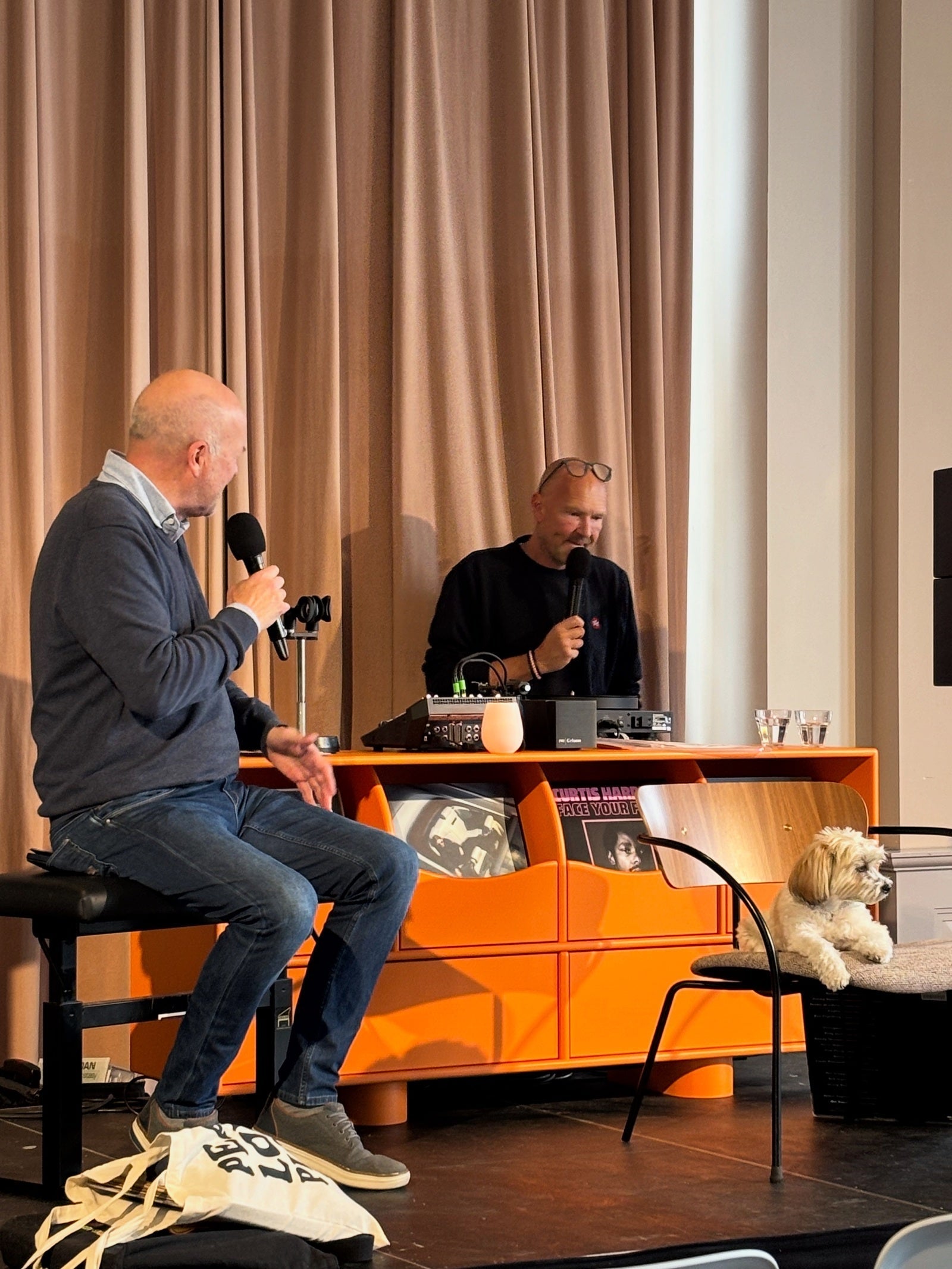 Twee sprekers tijdens het Haarlem Vinyl Festival bij een opvallende oranje platenkast met vinylplaten.
