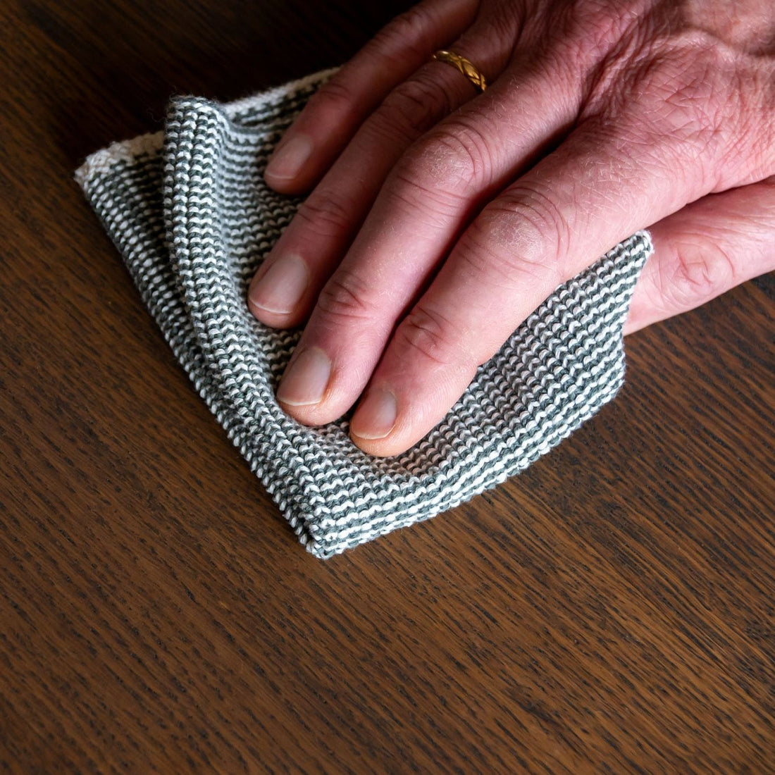 Handen reinigen het geoliede houten oppervlak van een platenkast voorzichtig met een zachte doek.
