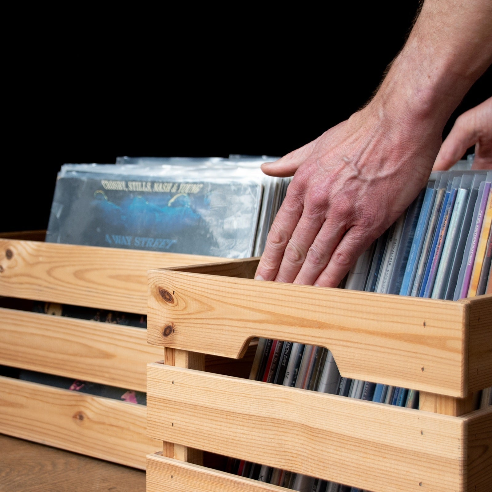 Handen bladeren door een lp-verzameling in houten platenkisten bij het beoordelen en verkopen van een vinylcollectie